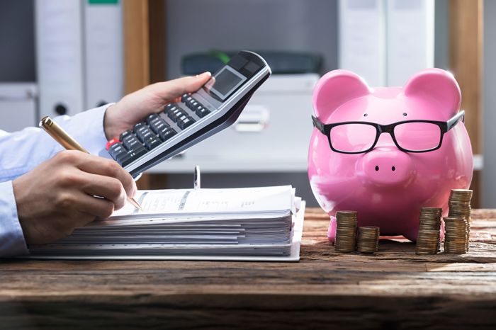 © Andrey Popov - stock.adobe.com Foto: Hände mit Aktenordner, Taschenrechner und Sparschwein
